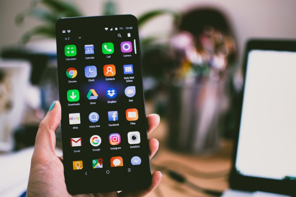 A hand holding a smartphone showing app icons on the home screen.