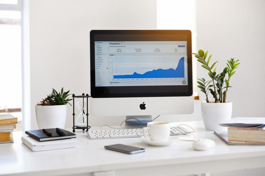 A clean workspace with a desktop computer showing analytics, surrounded by plants, books, and a coffee cup.