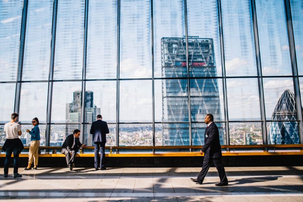People in a modern office lobby with a large glass window overlooking city skyscrapers.